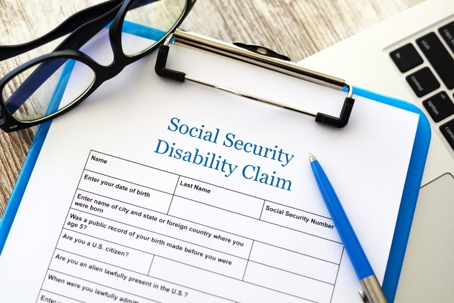 Social Security Disability Claim form on a clipboard with a pen, glasses, and part of a laptop on a desk. | Zen Law Firm