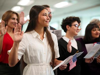 A group of people hold their right hands up while holding US flags and oaths.